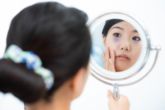 血流が悪く、目の下の青ぐまができている女性が手鏡をのぞいている