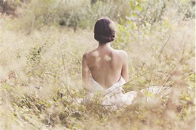 野原でヨガをする女性。背中が見える白い服を着ていて、美しい背中をしている。